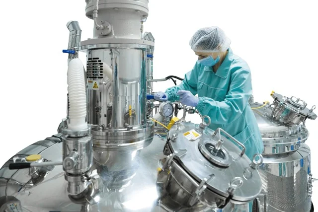 Technician working with a stainless steel reactor in a clean production room